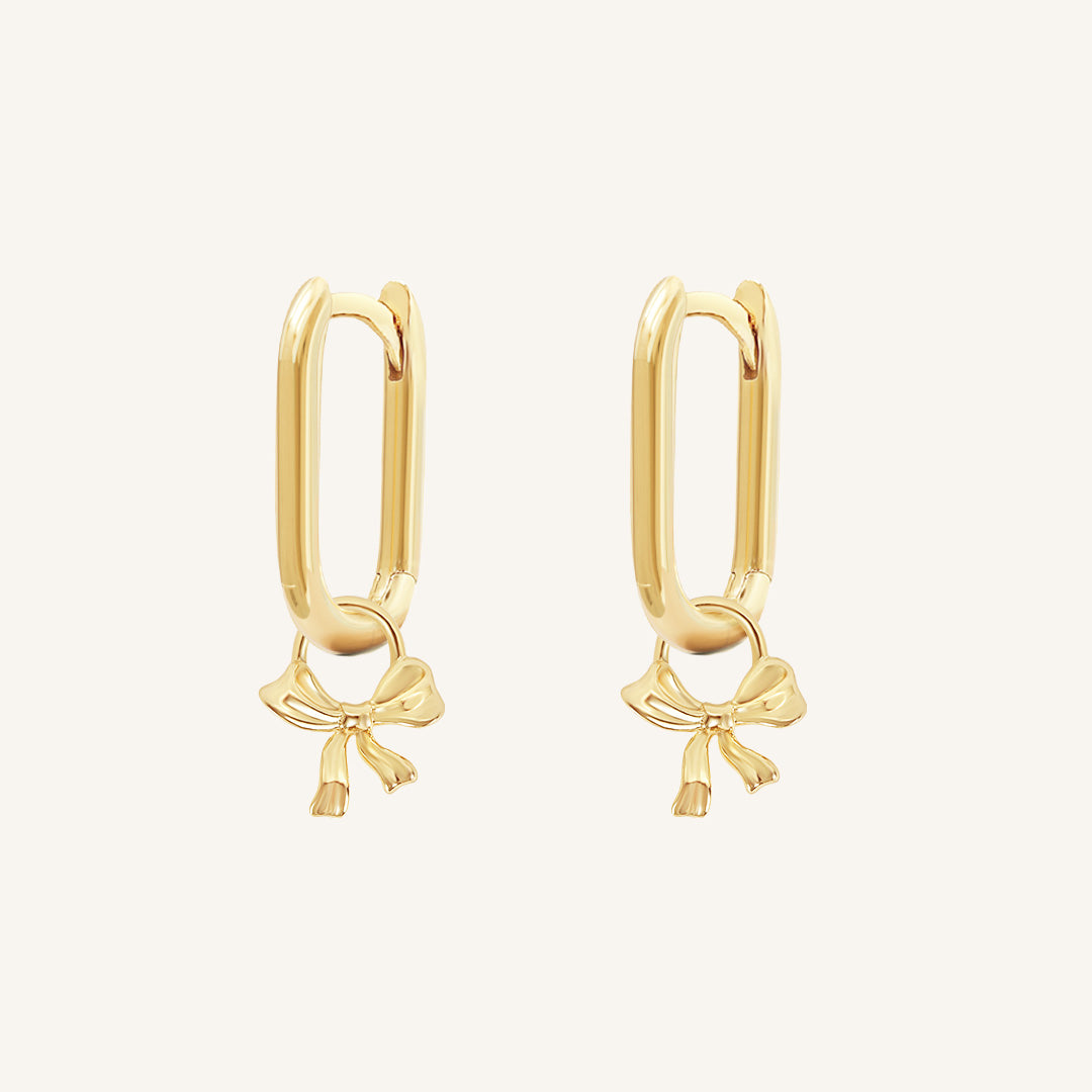 A pair of gold-tone hoop earrings with a charm in the shape of a rectangle bow.