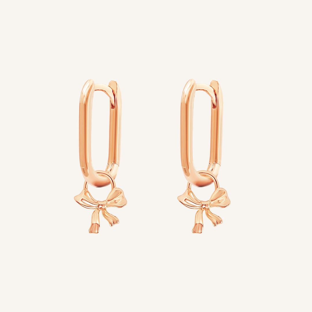 A pair of gold-tone charm hoop earrings with a simple bow design.