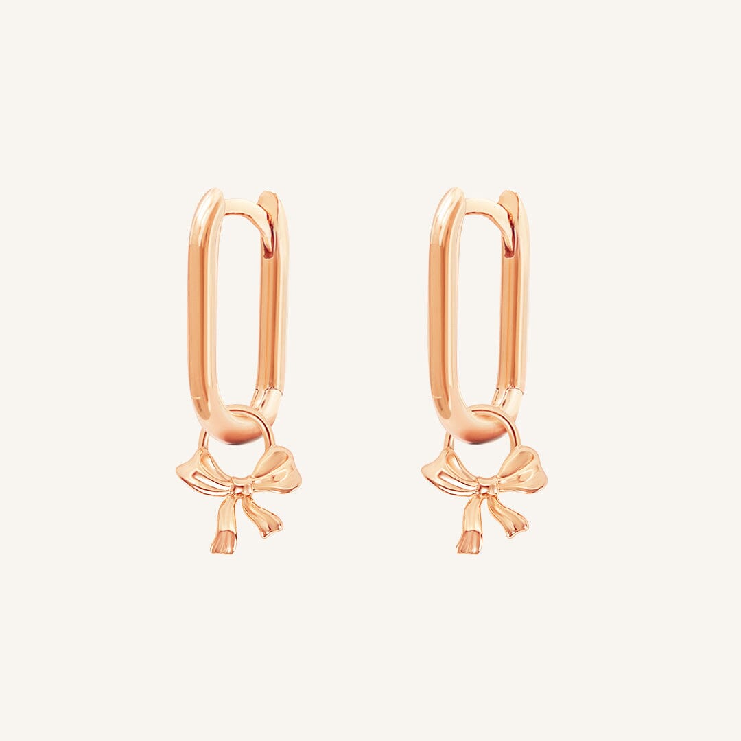 A pair of gold-tone charm hoop earrings with a simple bow design.