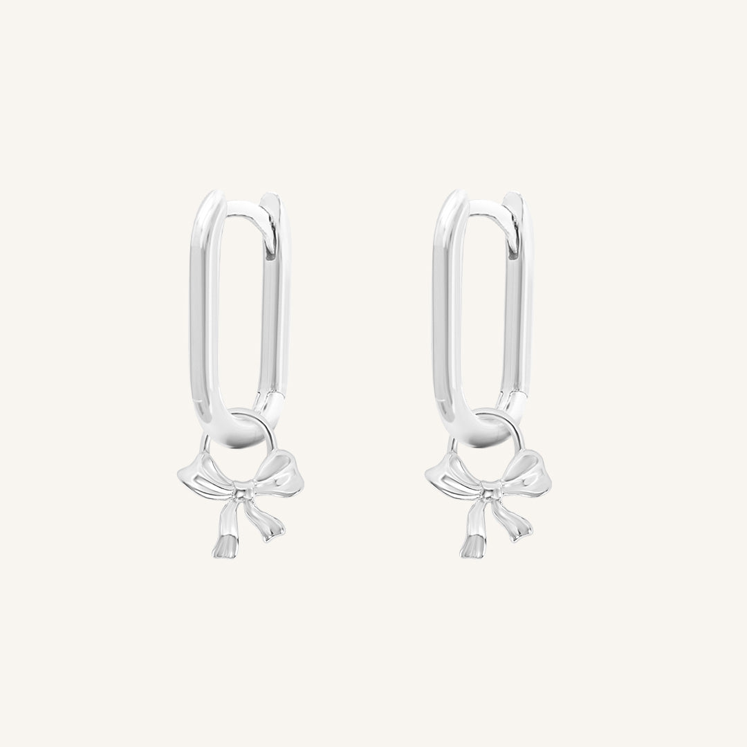 A pair of silver-tone charm hoop earrings with a simple bow design.