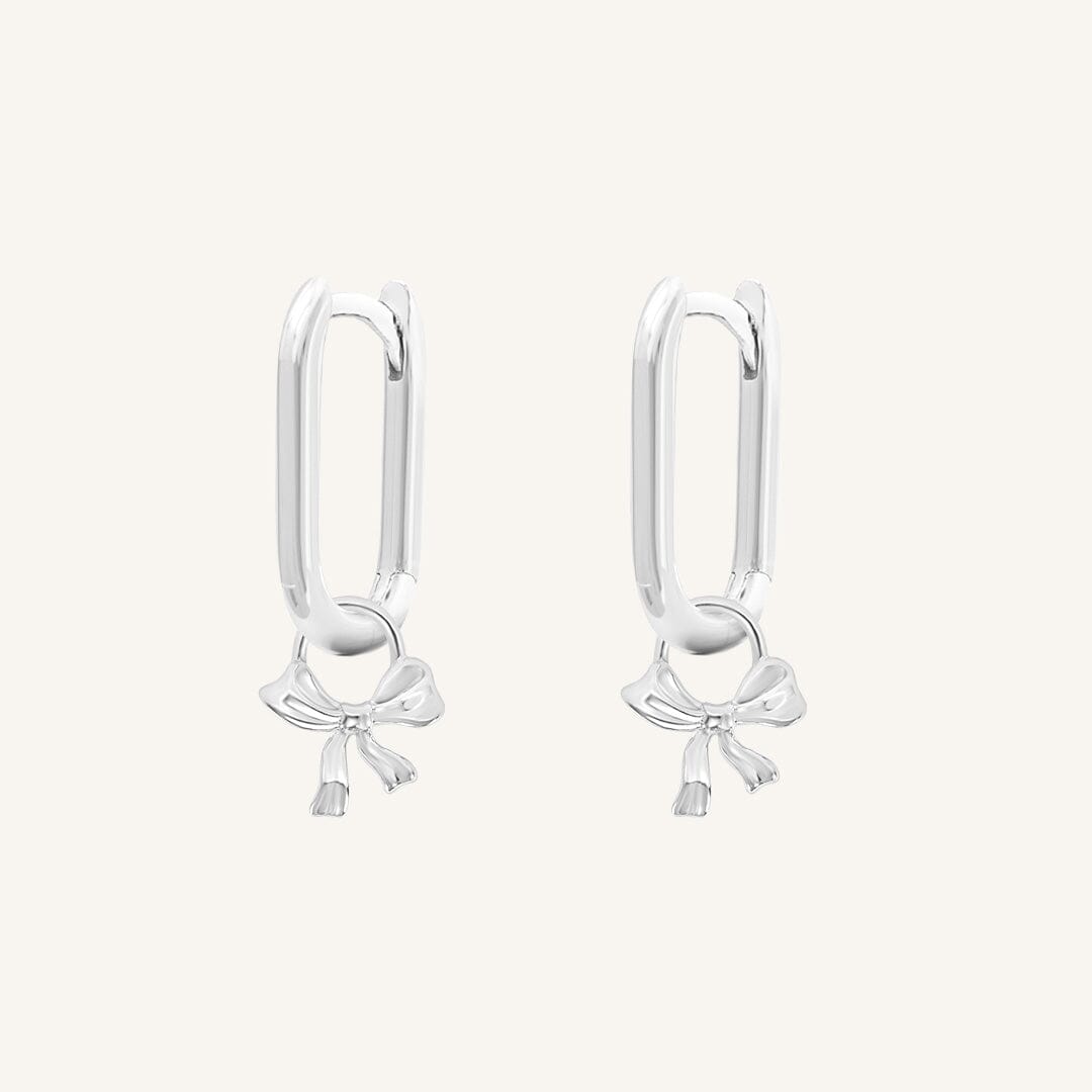 A pair of silver-tone charm hoop earrings with a simple bow design.