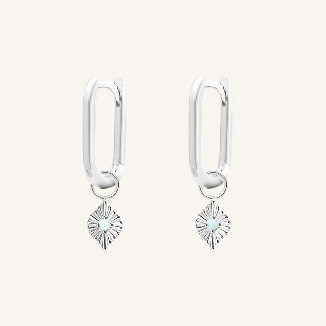 A pair of silver hoops with diamond shaped hoop charms featuring a faux opal, worn by model