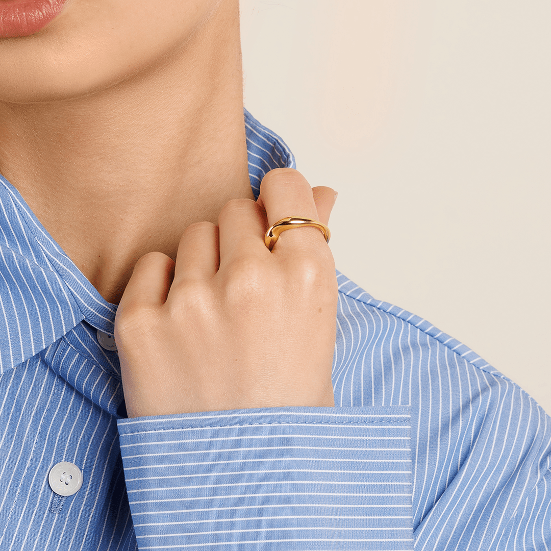 A gold-coloured ring with an irregular, smooth shape worn on finger