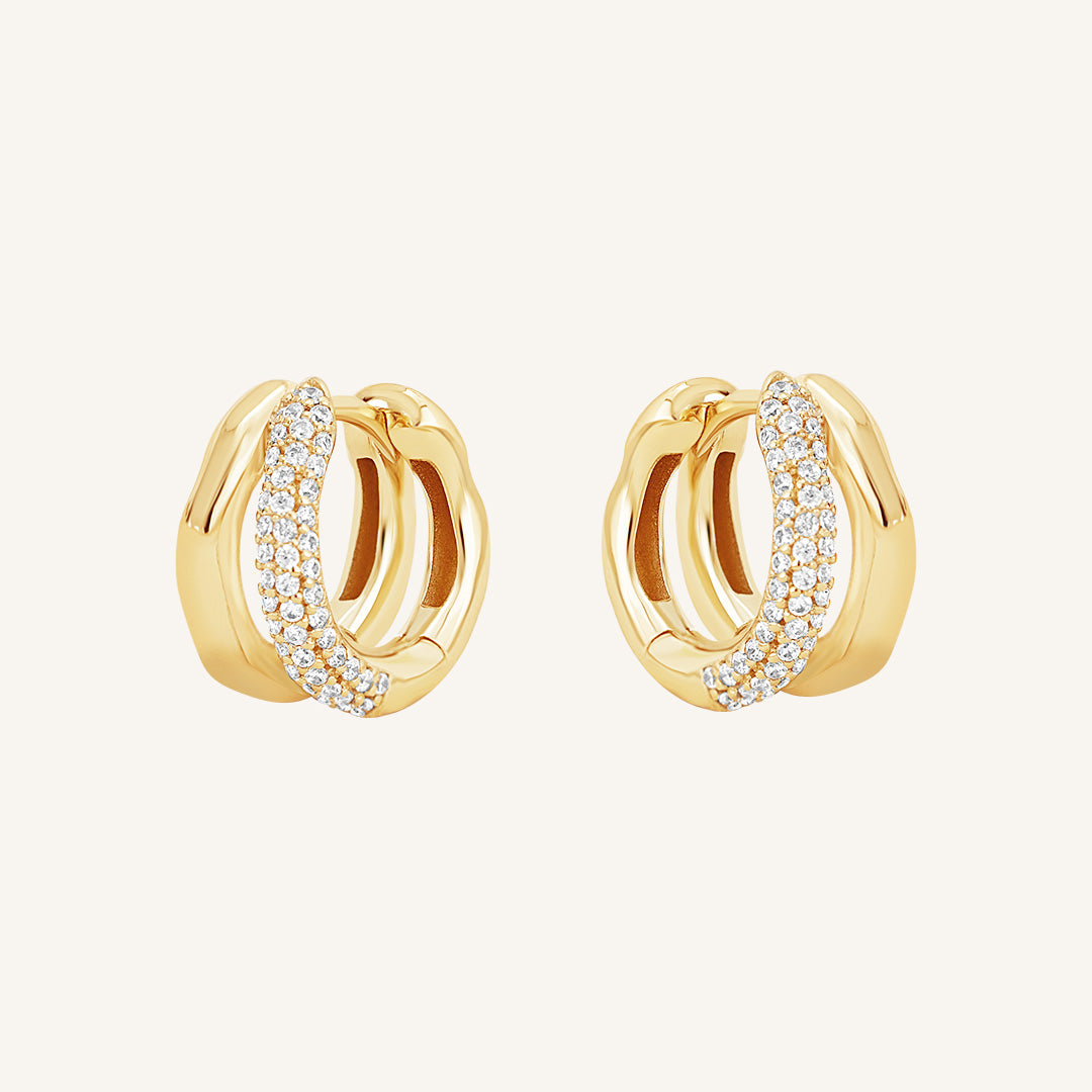 A pair of gold-coloured hoop earrings with a huggie design, featuring a layered look and pave white stones on one side.