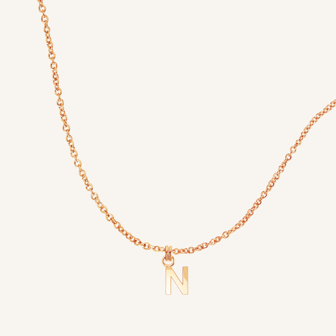 Rose gold necklace with a 'N' pendant on a light beige background