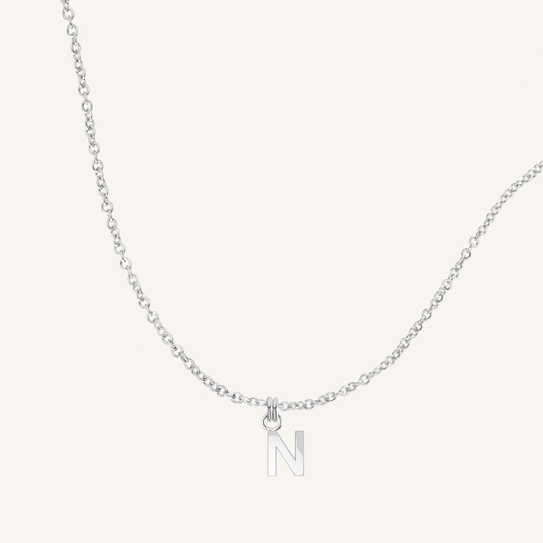 Silver necklace with a 'N' pendant on a light gray background