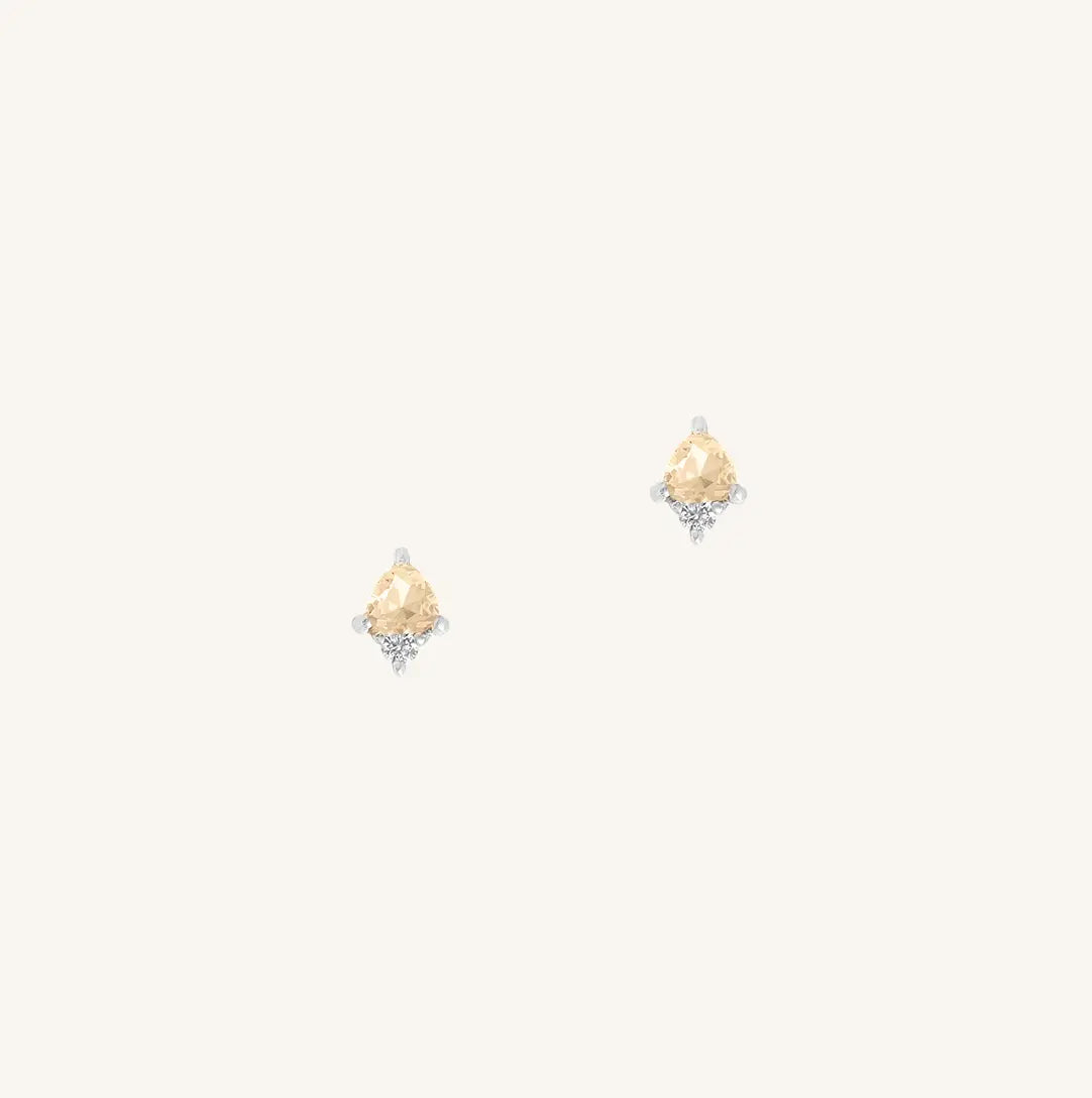 A silver pair of stud earrings featuring a citrine cubic zirconia, representing November.
