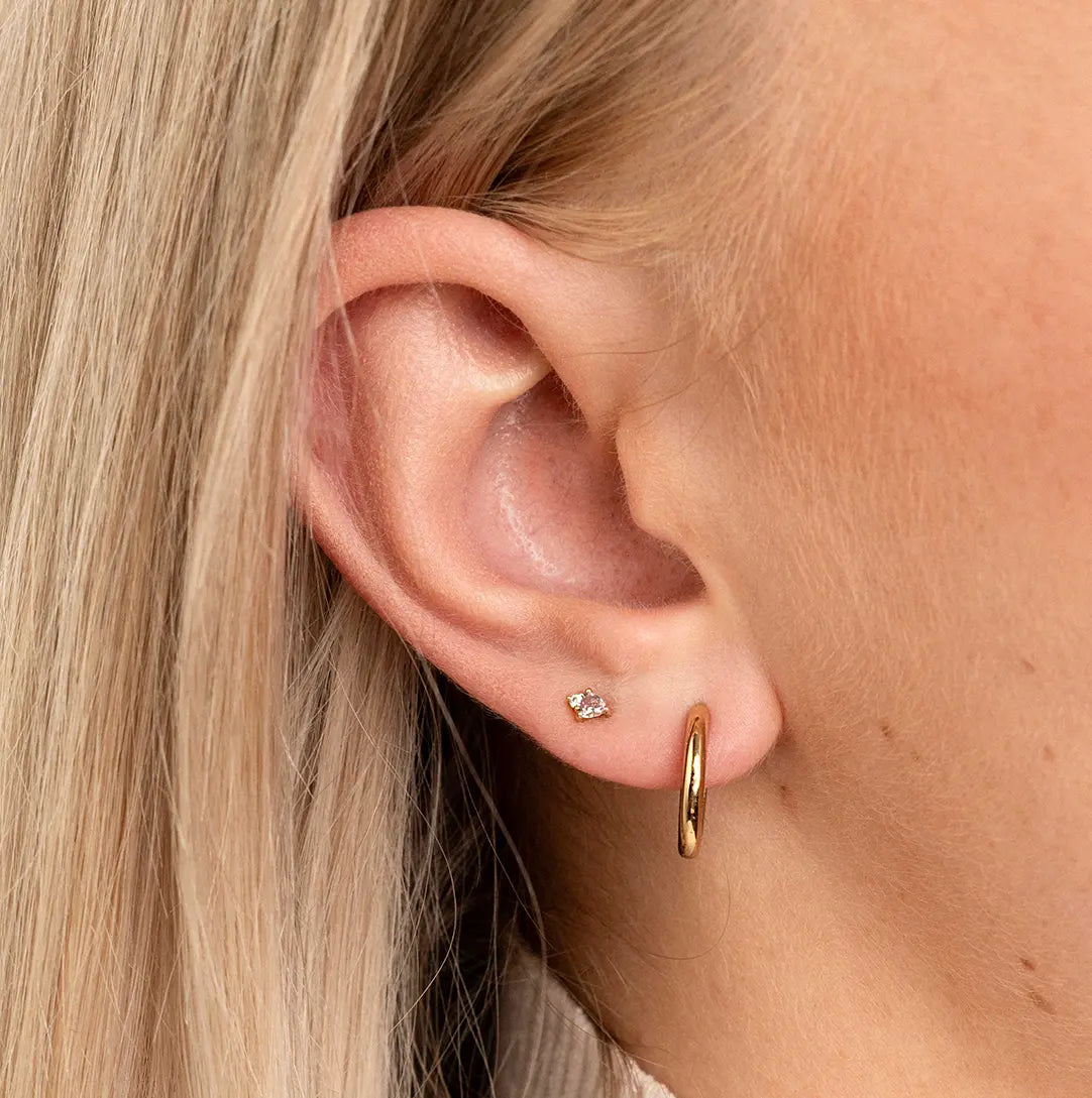 A gold pair of stud earrings featuring a citrine cubic zirconia, representing November, worn in ear