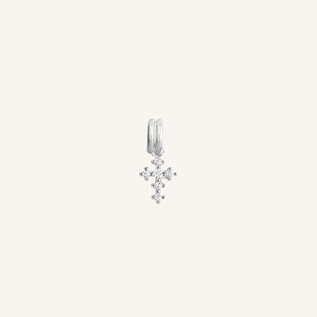A petite silver cross charm with cubic zirconia on white background