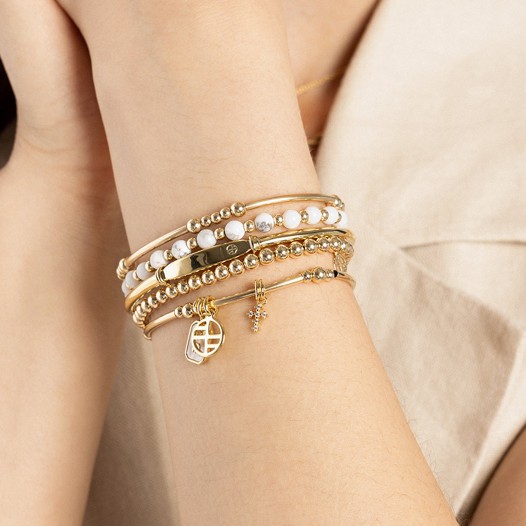 A petite gold cross charm with cubic zirconia attached to bracelet, on wrist