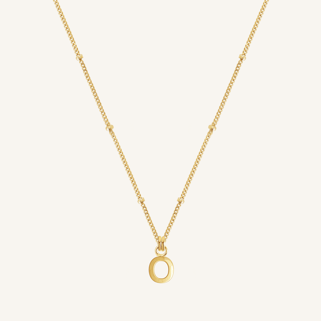 Gold necklace with an O pendant on a light beige background