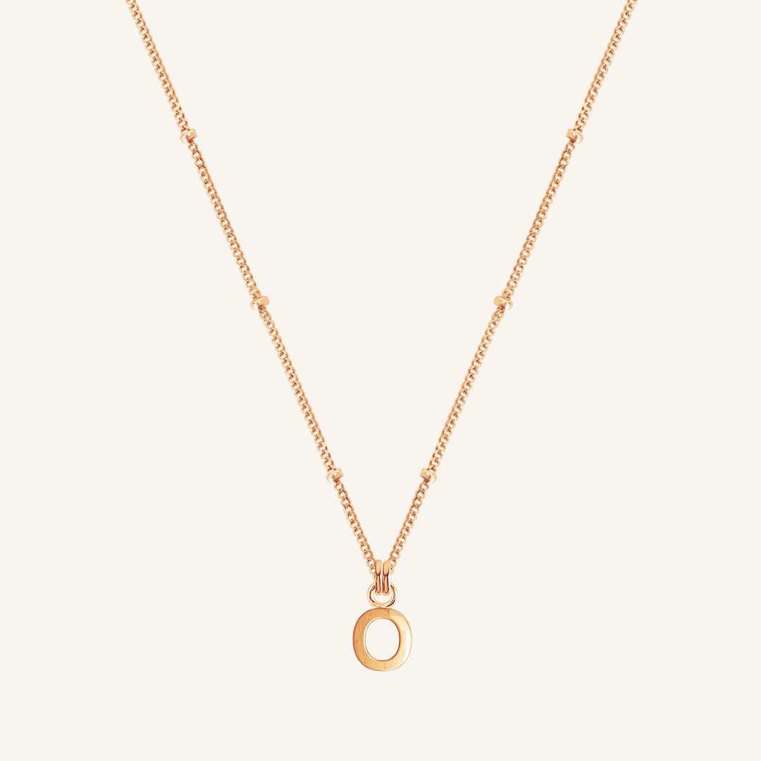 Rose gold necklace with an 'O' pendant on a light beige background