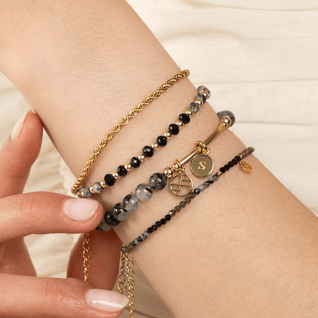 A gold-tone rope bracelet with a extender chain, layered with bracelets, on the wrist