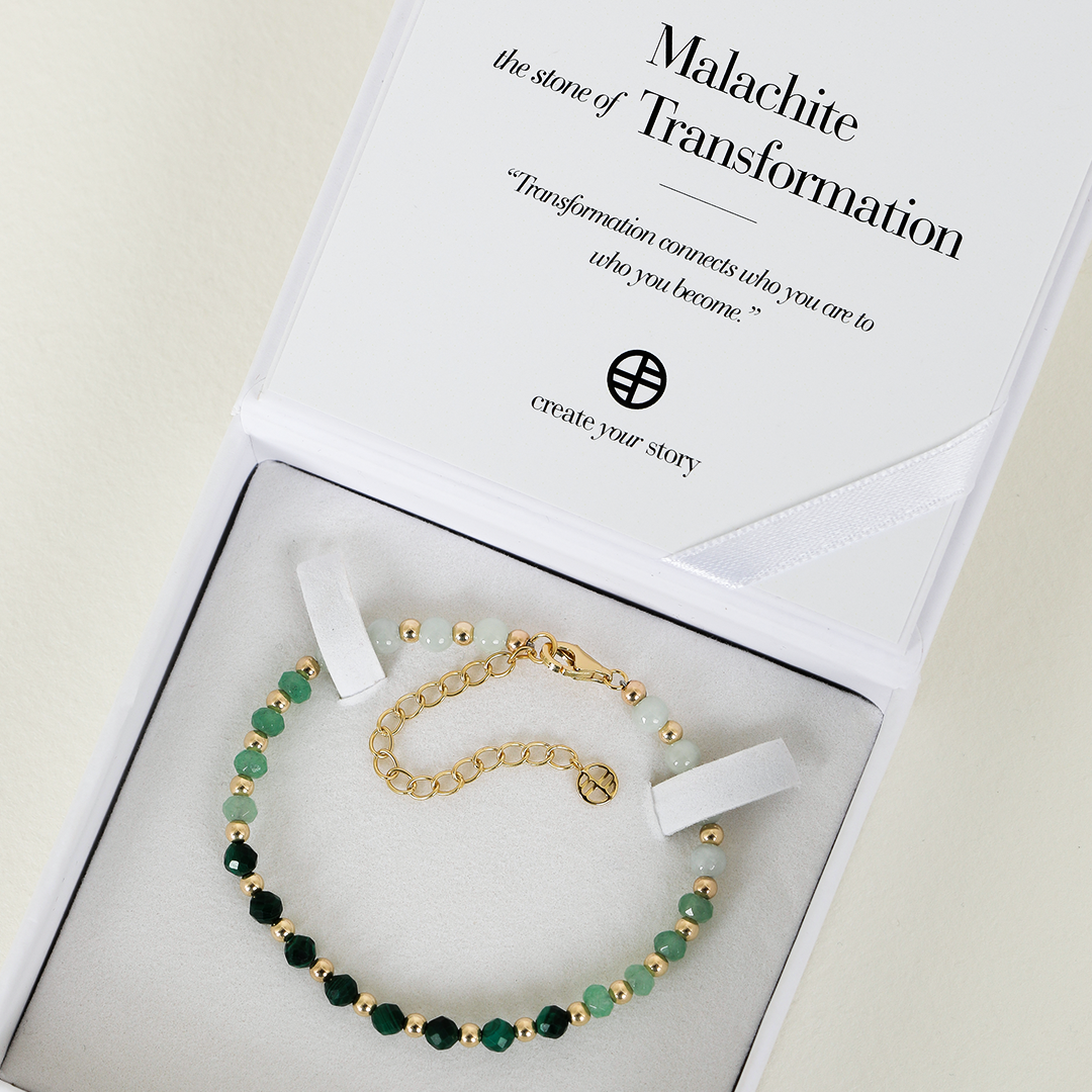 A beaded bracelet with green malachite ombre and gold metal accents, featuring an extender chain, displayed in box