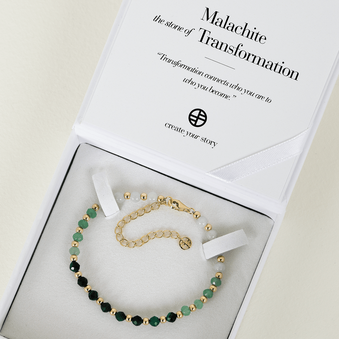 A beaded bracelet with green malachite ombre and gold metal accents, featuring an extender chain, displayed in box