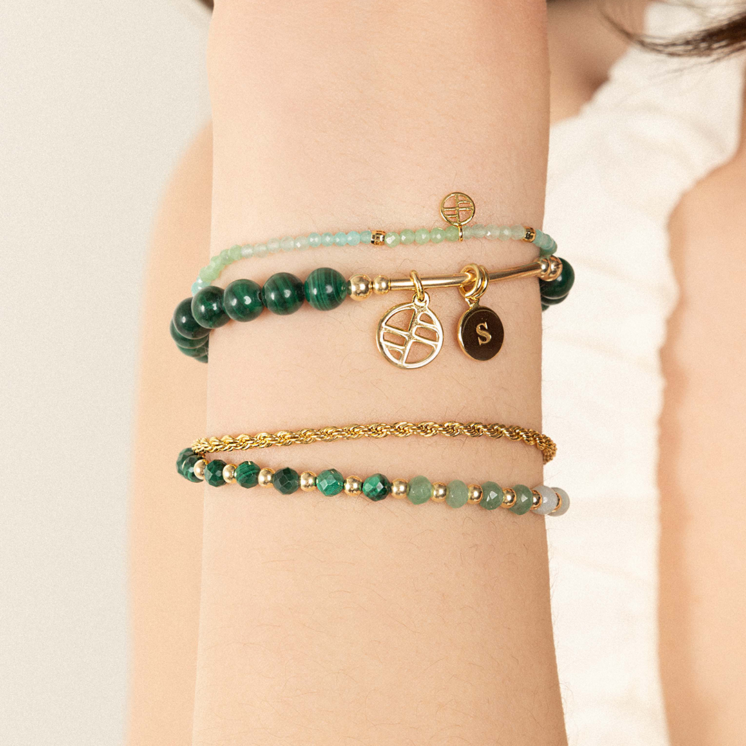 A beaded bracelet with green malachite ombre and gold metal accents, featuring an extender chain, worn on wrist