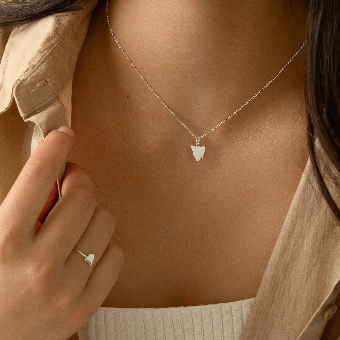 A silver-colored charm in the shape Tasmania, on silver chain, on models neck