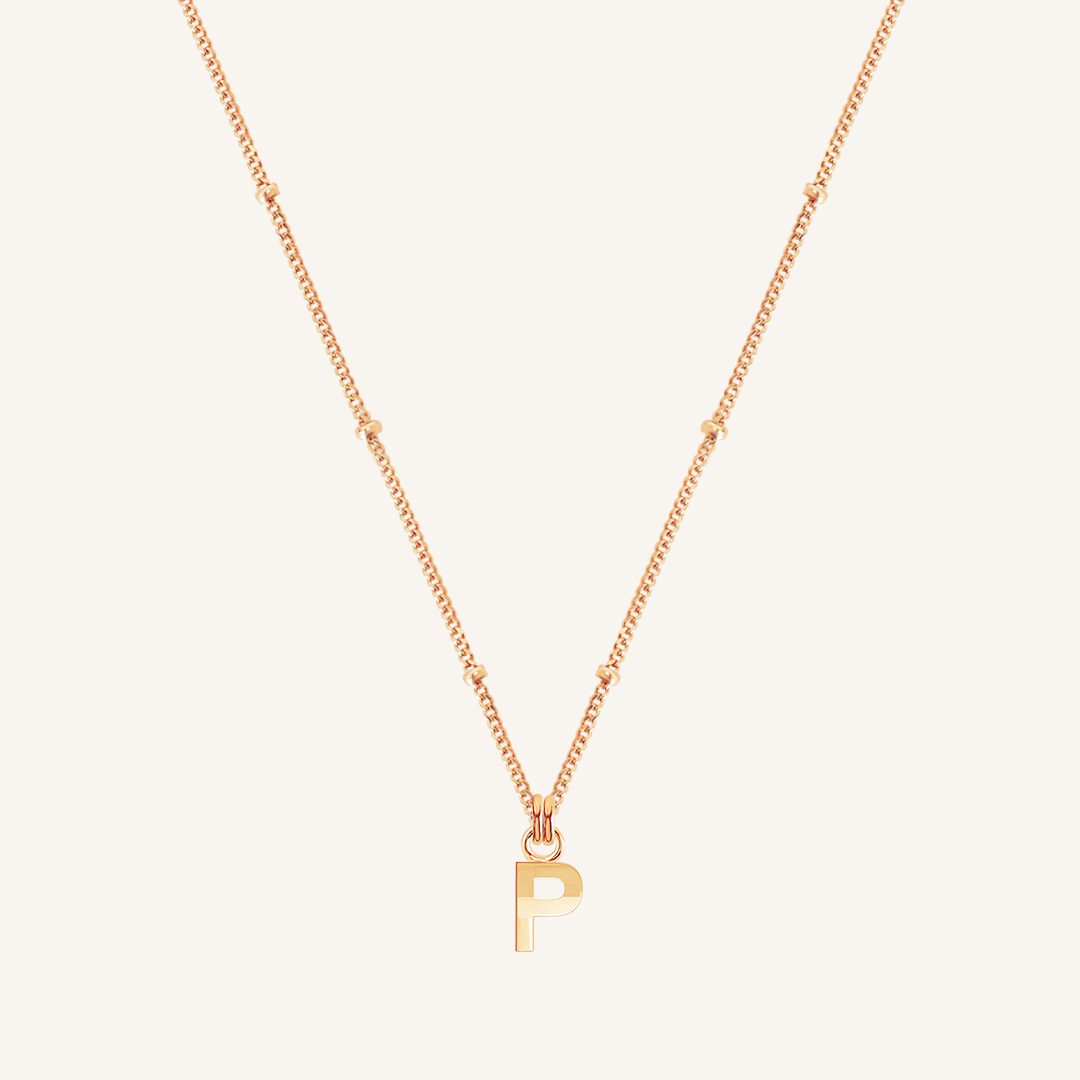 Rose gold necklace with a 'P' pendant on a light beige background