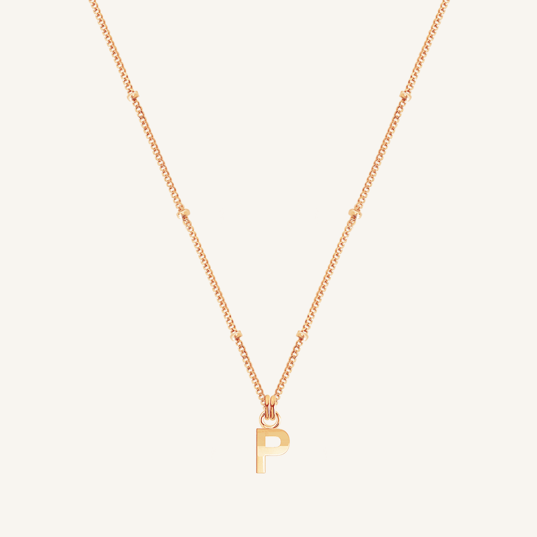 Rose gold necklace with a 'P' pendant on a light beige background