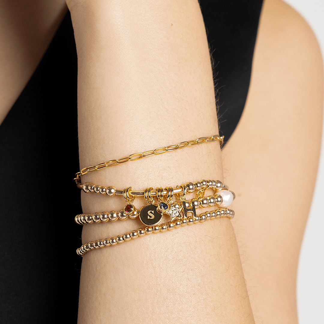 A gold-coloured bracelet with a luck star charm and small bead details worn on wrist, stacked with other gold bracelets