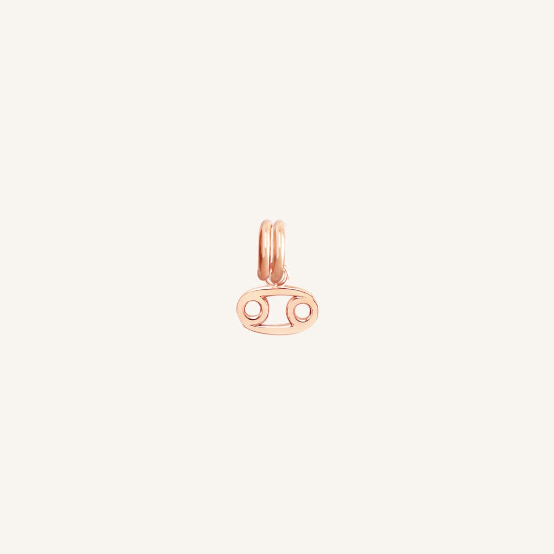 A small rose gold charm with the symbol for the zodiac sign Cancer.