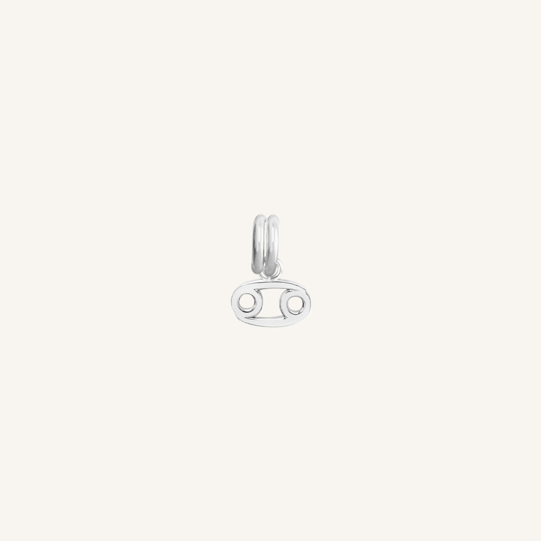 A small silver charm with the symbol for the zodiac sign Cancer.