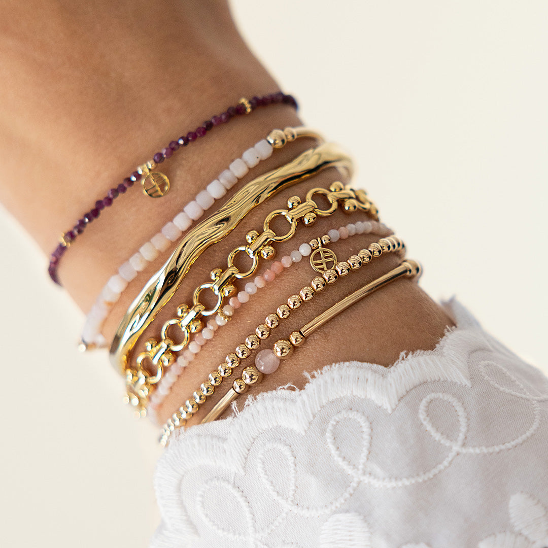 Close-up of a wrist wearing multiple gold and beaded bracelets on a light background