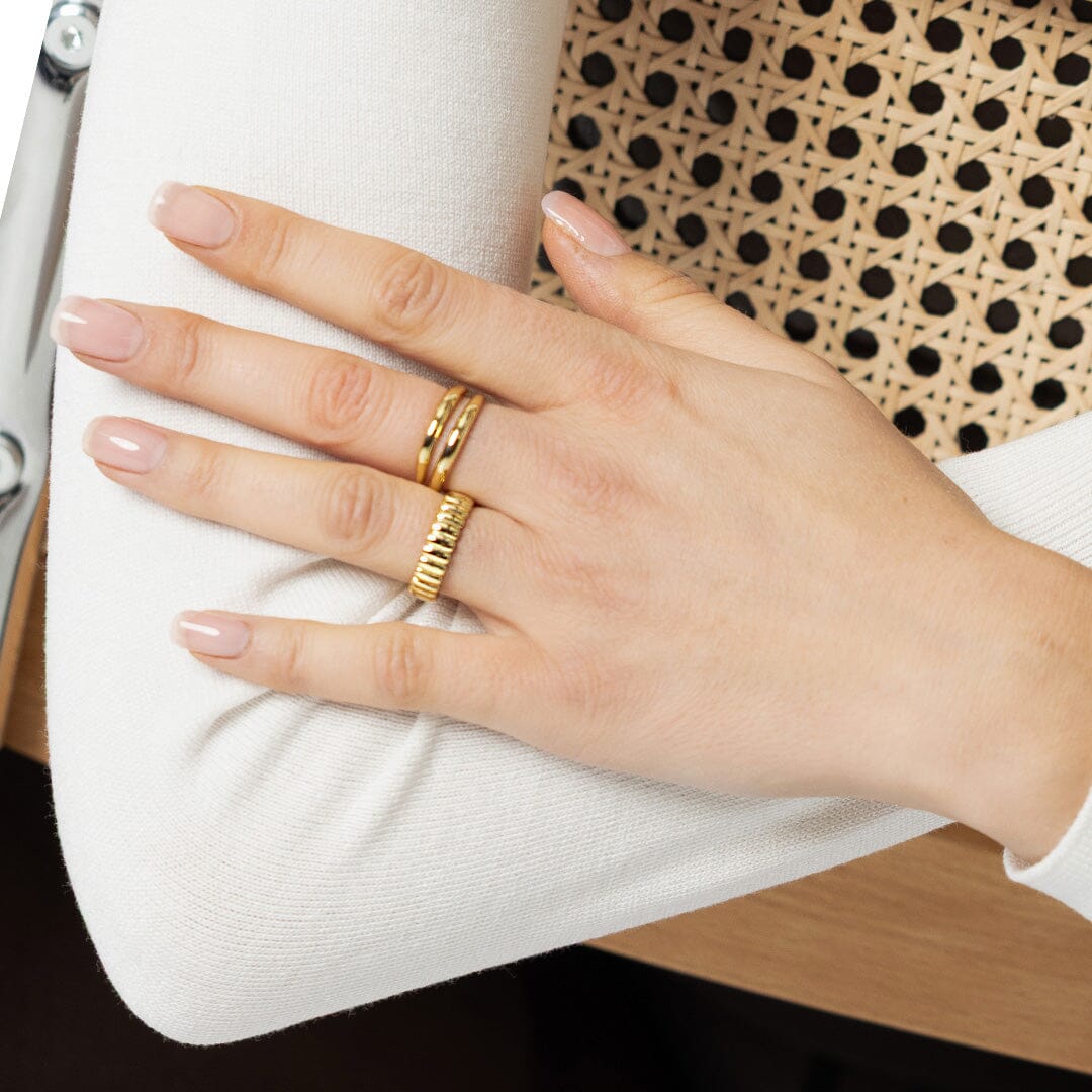 Hand wearing a gold ring on a white surface with a polka dot pattern in the background
