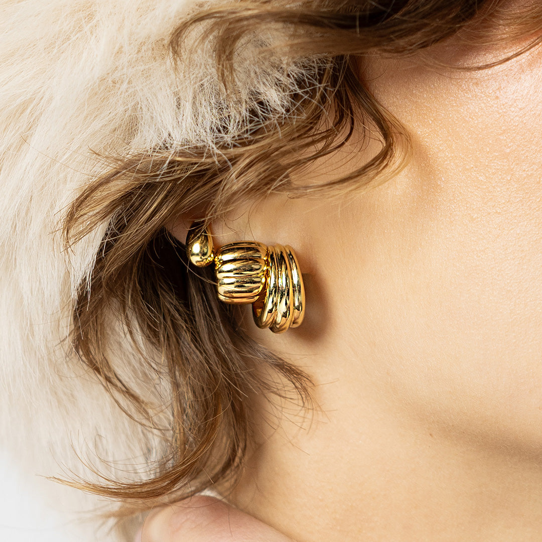 Gold hoop earrings worn by a person with light skin and blonde hair.
