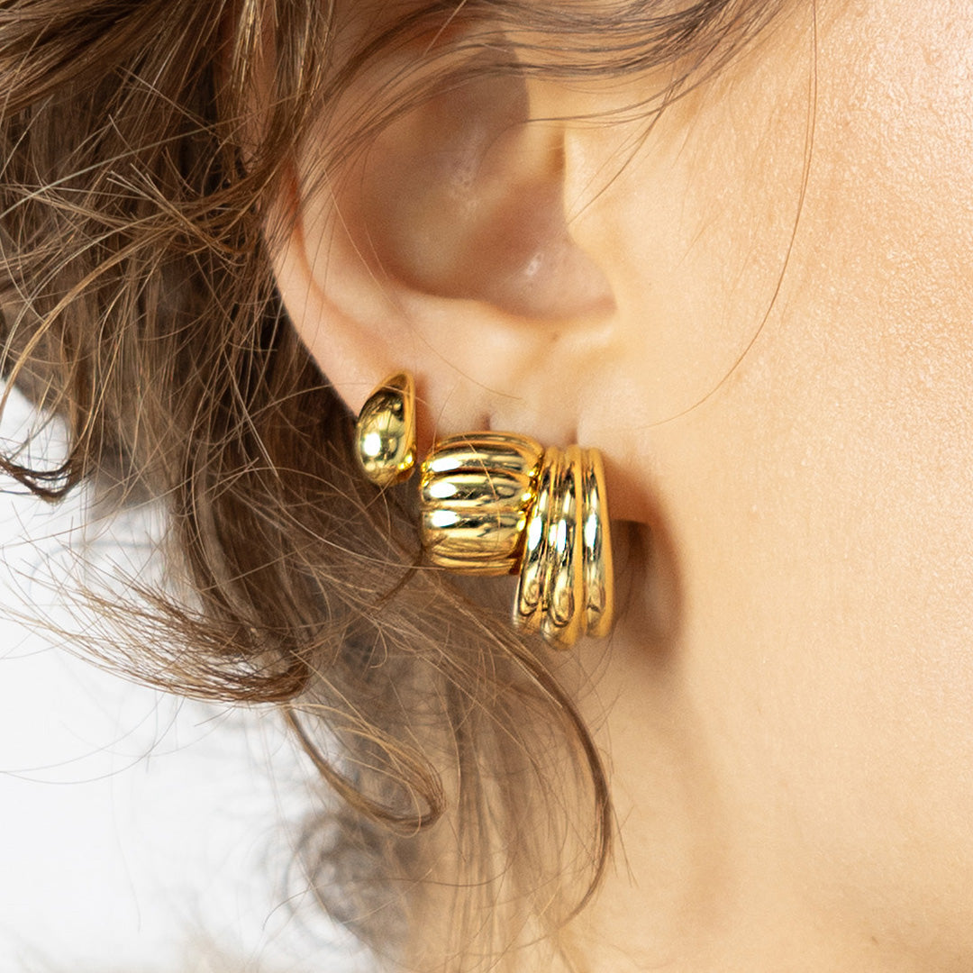 Close-up of a person wearing gold hoop earrings with a blurred background