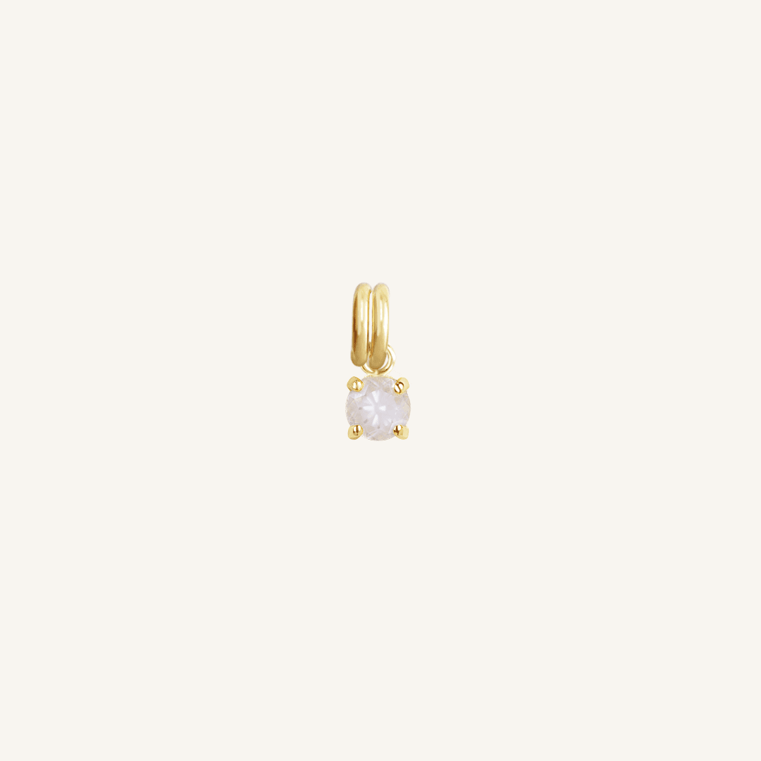 A small gold-colored charm with a moonstone, designed to attach to a bracelet or necklace