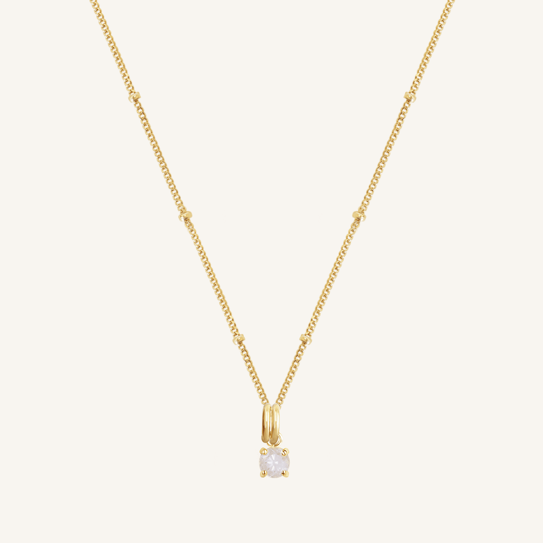 A gold-tone charm necklace with a small moonstone pendant, isolated on a white background.