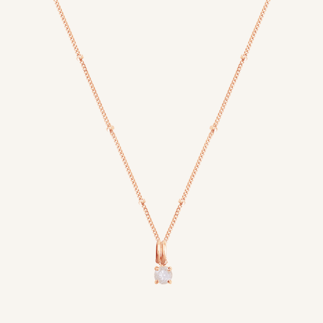 A rose charm necklace with a small moonstone pendant, isolated on a white background.