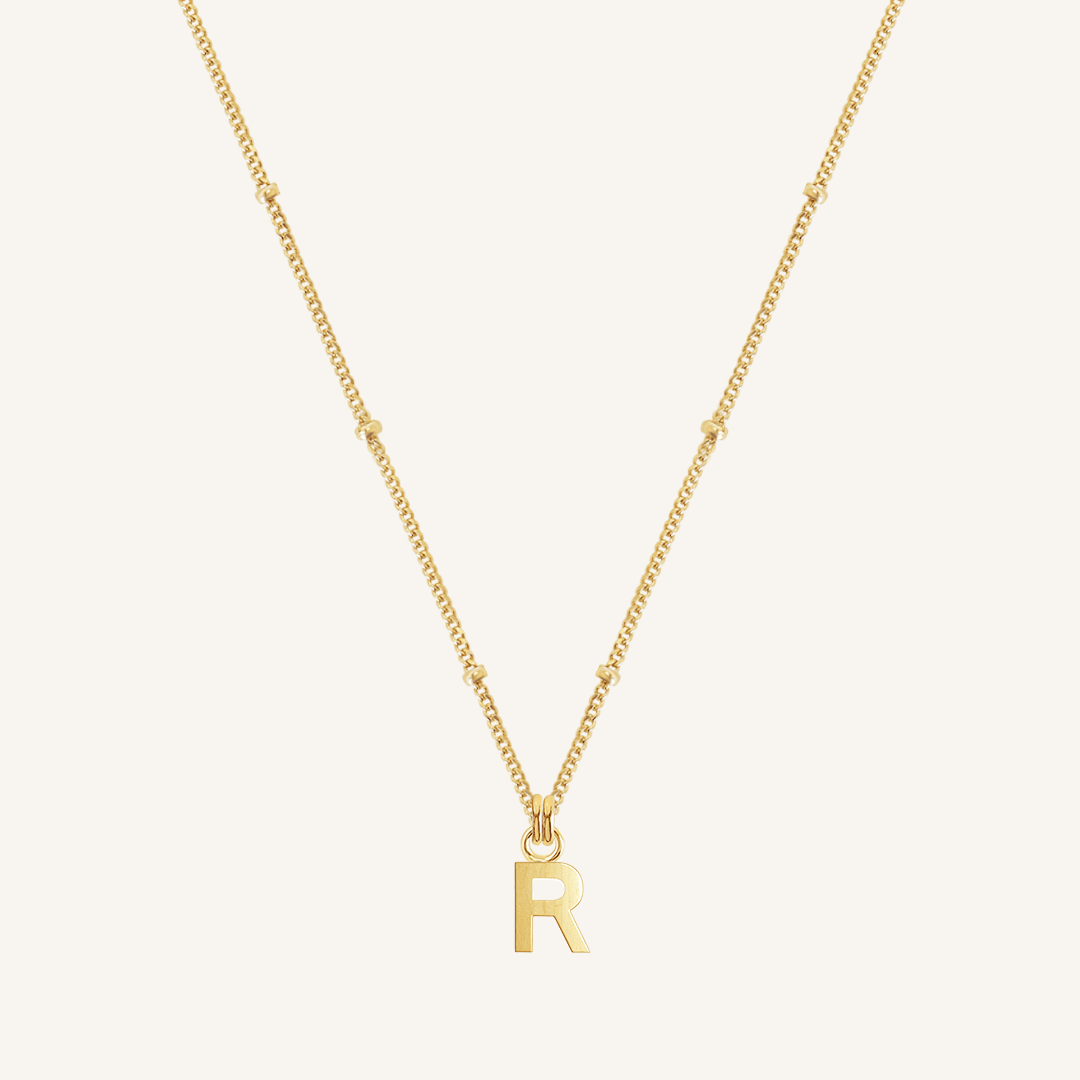 Gold necklace with 'R' pendant on a white background