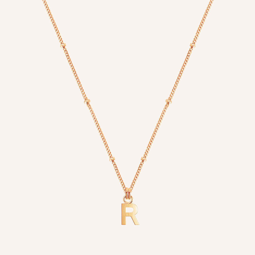 Gold necklace with 'R' pendant on a light beige background