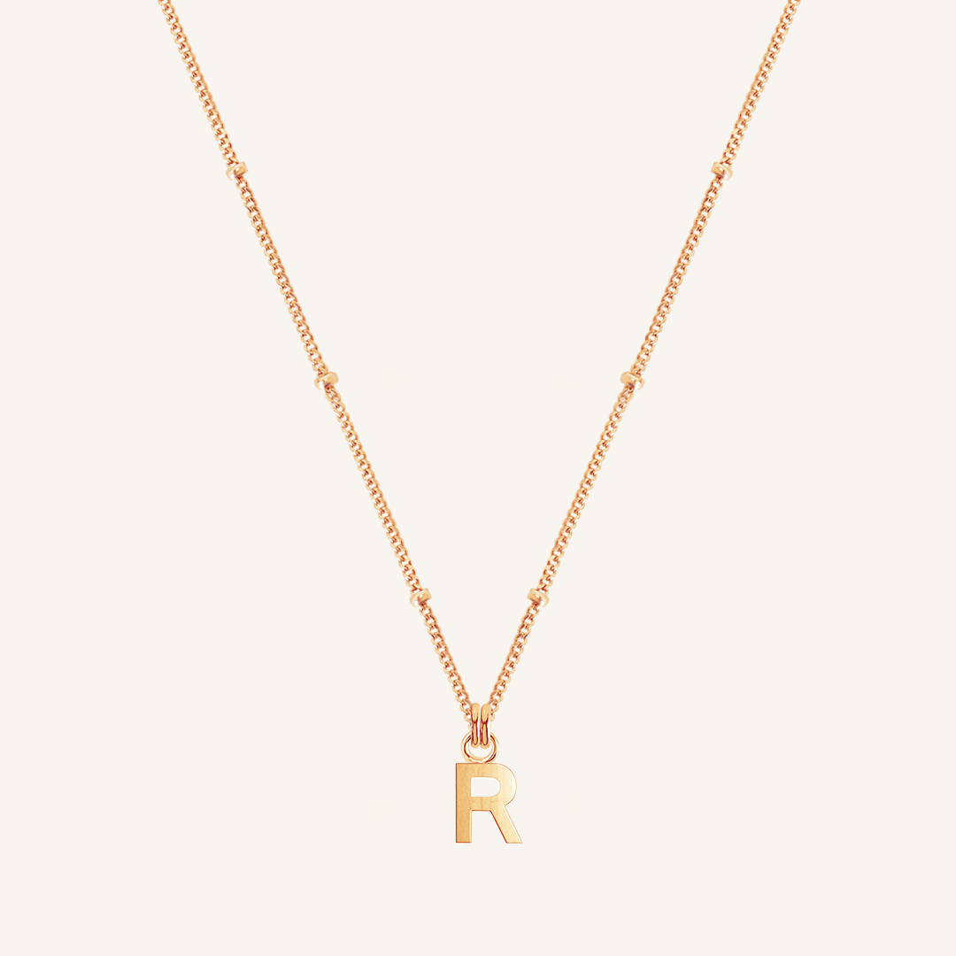 Gold necklace with 'R' pendant on a light beige background