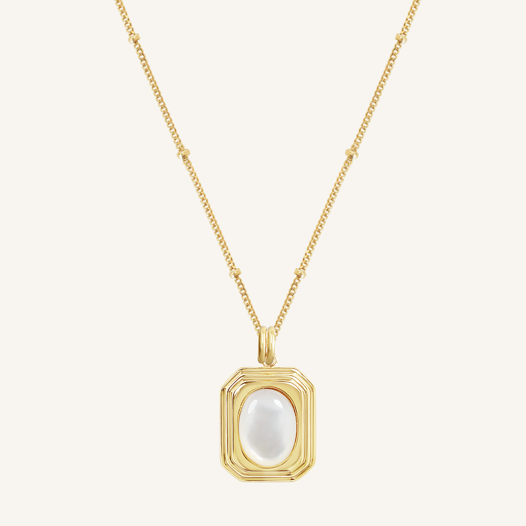 A gold-tone necklace with a large mother-of-pearl pendant on a chain.