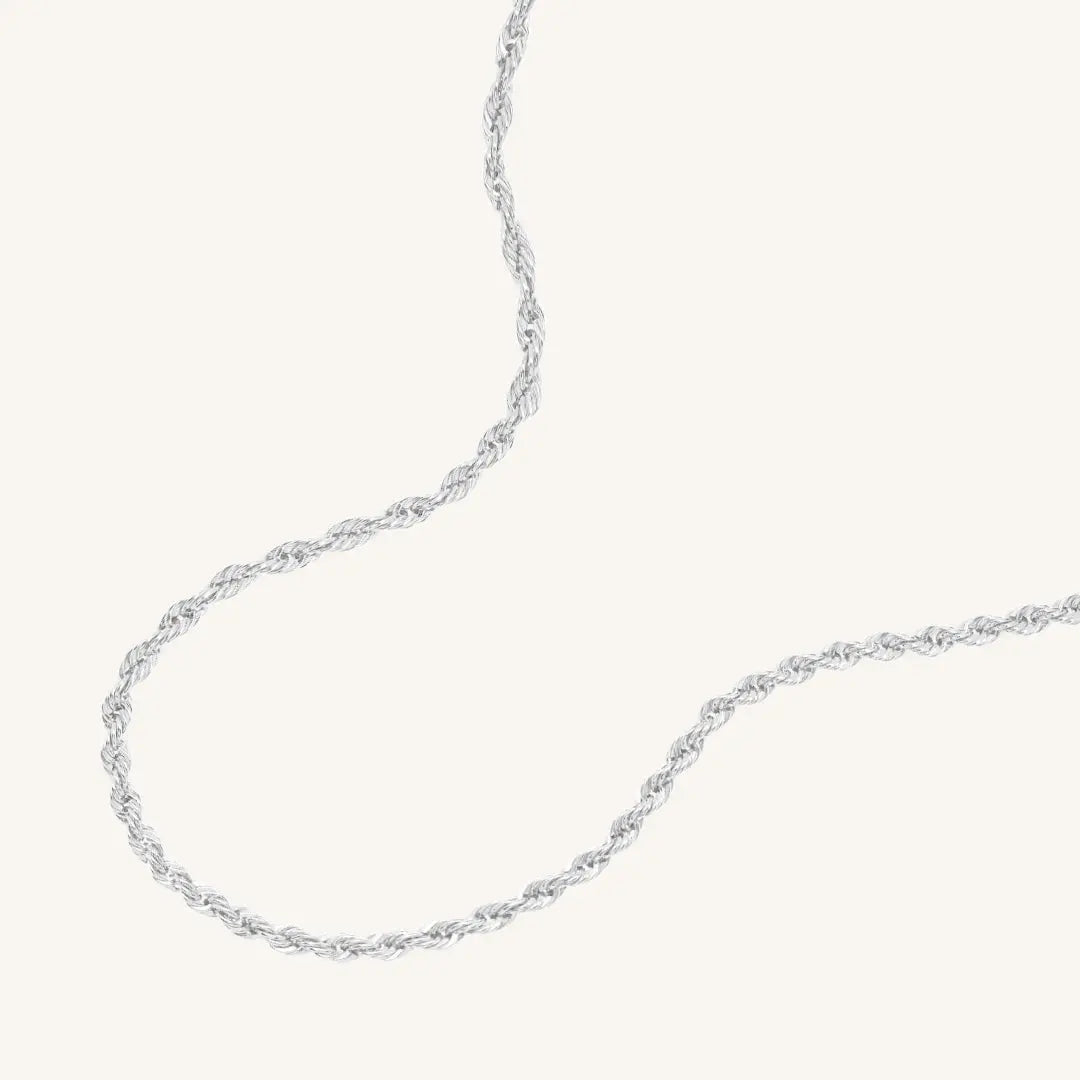 A silver rope chain necklace on a plain background.