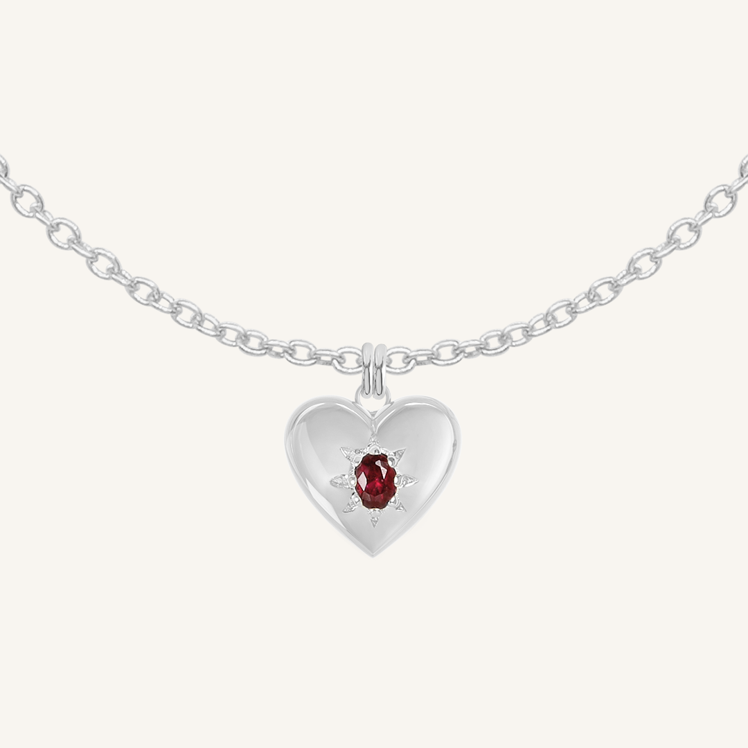 silver heart shaped charm with deep red oval cubic zirconia on plain chain on white background