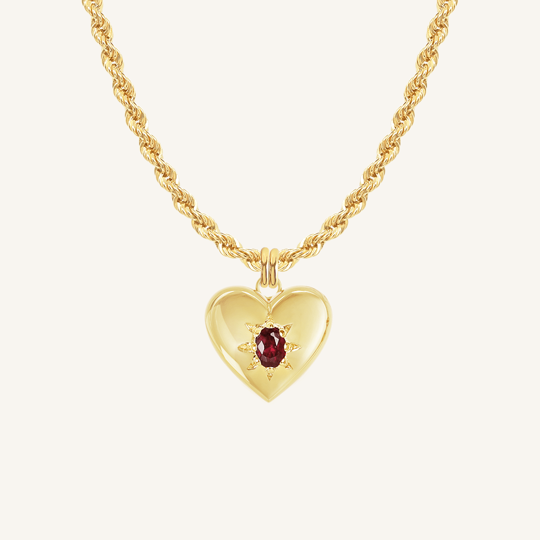 gold heart shaped charm with deep red oval cubic zirconia on rope chain on white background