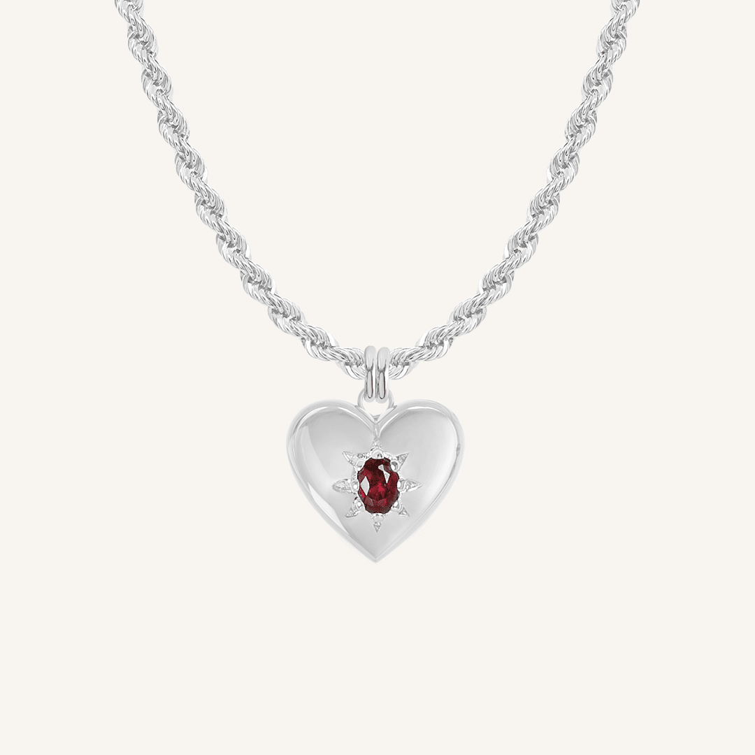 silver heart shaped charm with deep red oval cubic zirconia on rope chain on white background