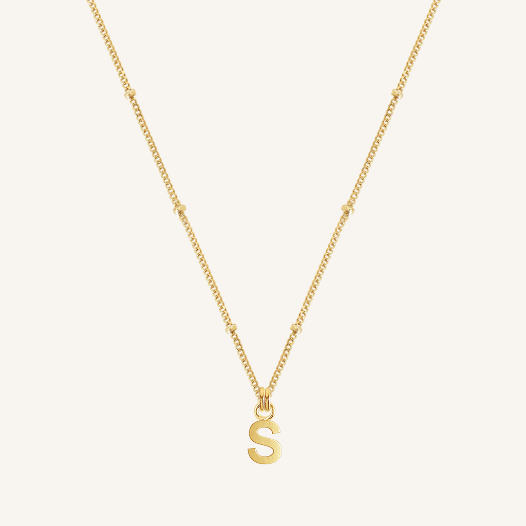 Gold necklace with a 'S' pendant on a light beige background
