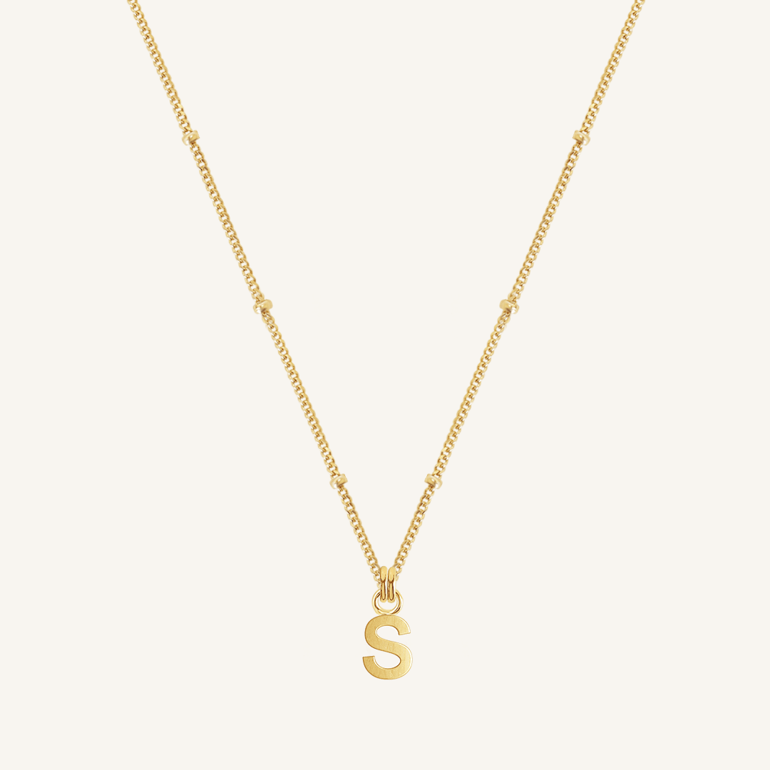Gold necklace with a 'S' pendant on a light beige background