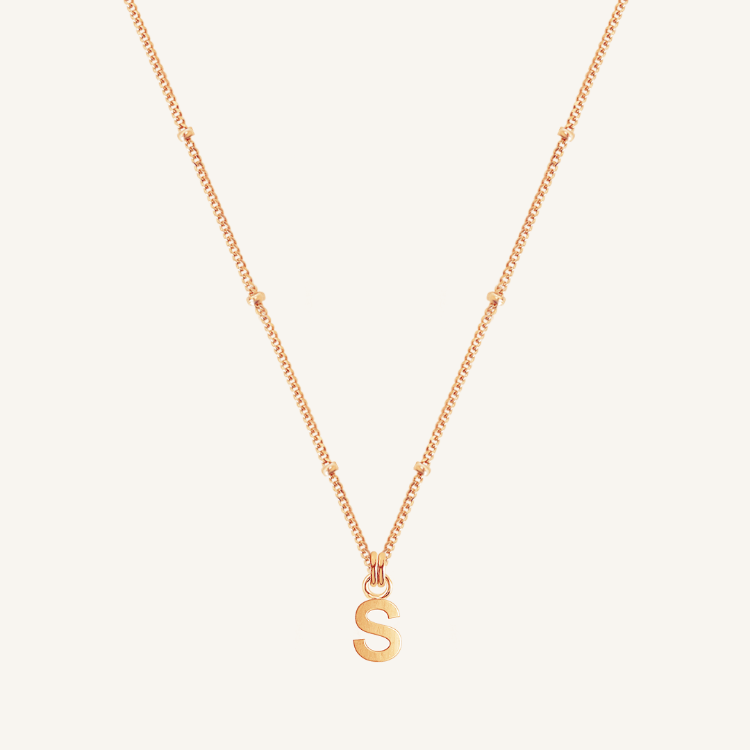 Gold necklace with a 'S' pendant on a light beige background