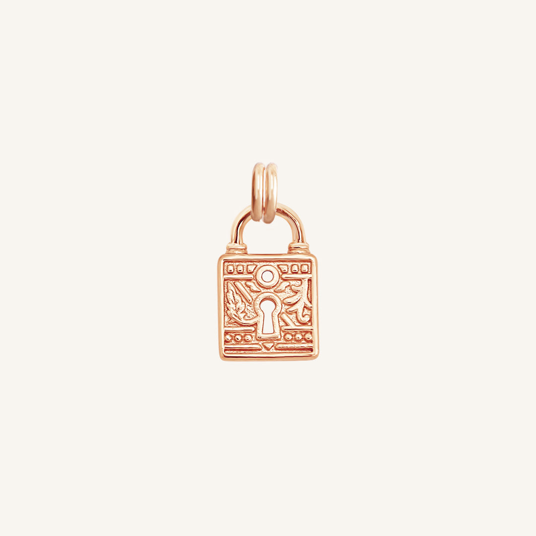 A rose-colored charm in the shape of a keylock with intricate patterns.