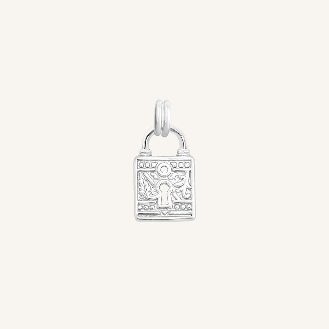 A silver-colored charm in the shape of a keylock with intricate patterns.