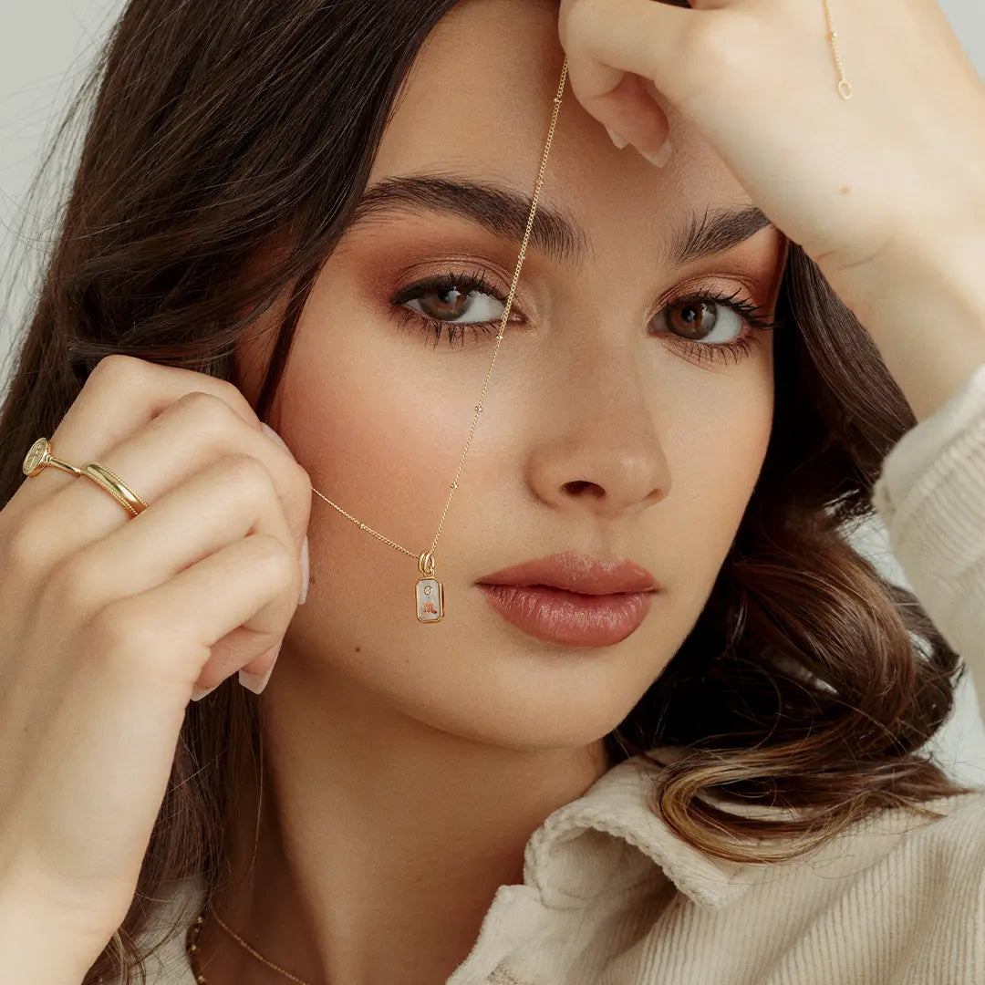A gold iridescent zodiac charm representing the Scorpio sign, with a loop for attachment on a chain, held by model