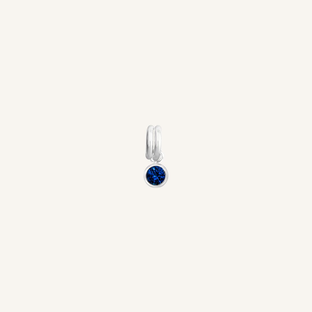 A round September birthstone charm with a blue cubic zirconia, set in silver.