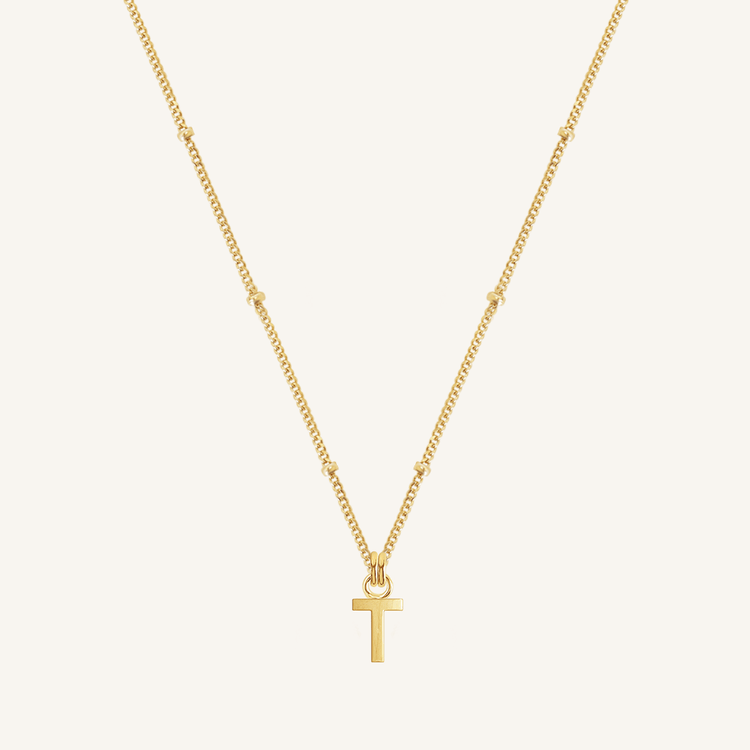 Gold necklace with a 'T' pendant on a light beige background