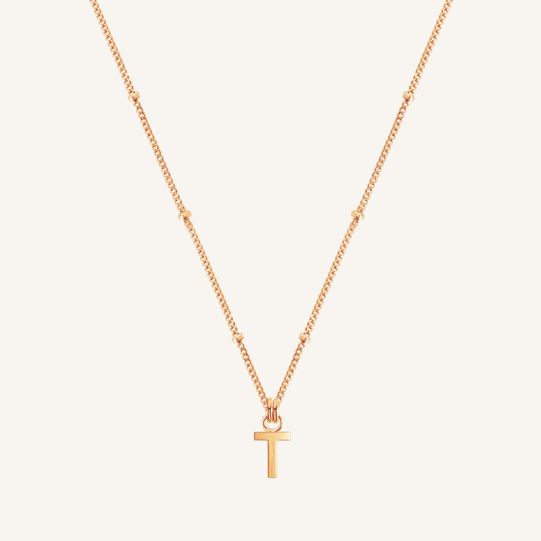 Rose gold necklace with a 'T' pendant on a light beige background
